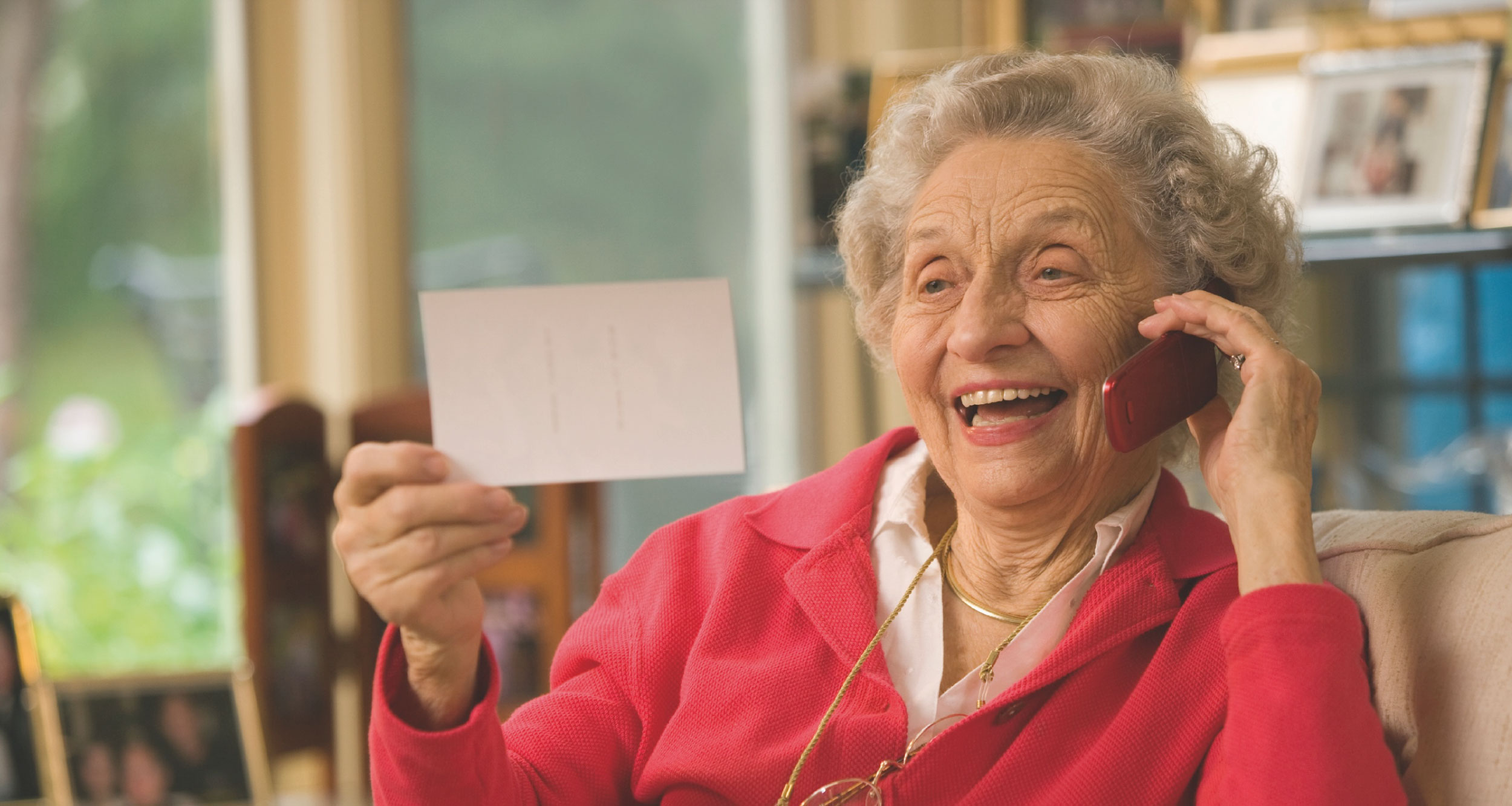 Seniorin im roten Oberteil telefoniert entspannt mit ihrer Familie
