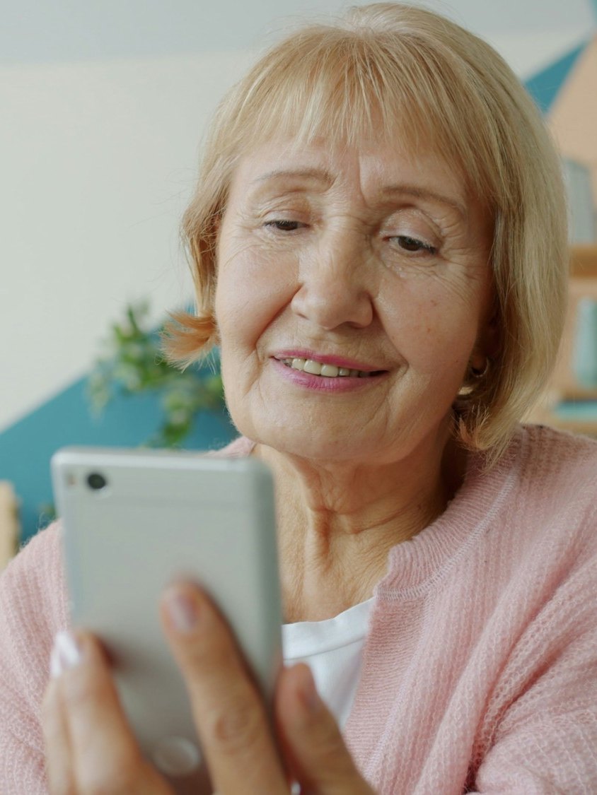 Seniorin sitzt im Wohnbereich und schaut auf ihr Smartphone